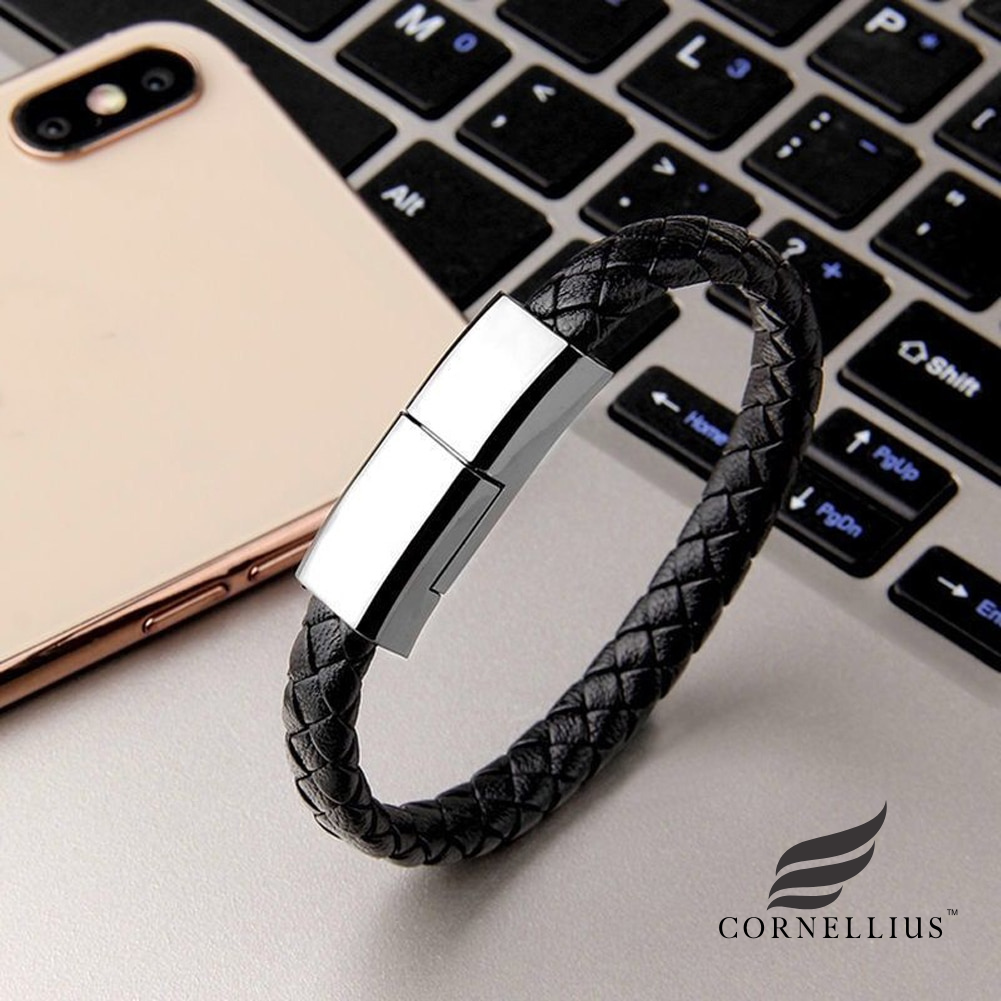 Bracelet câble de charge USB noir avec une boucle en acier inoxydable devant un ordinateur de type mac et un smartphone